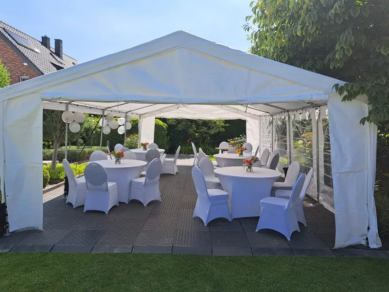 Offenes Partyzelt im Garten mit runden Tischen und Stühlen in weißen Hussen