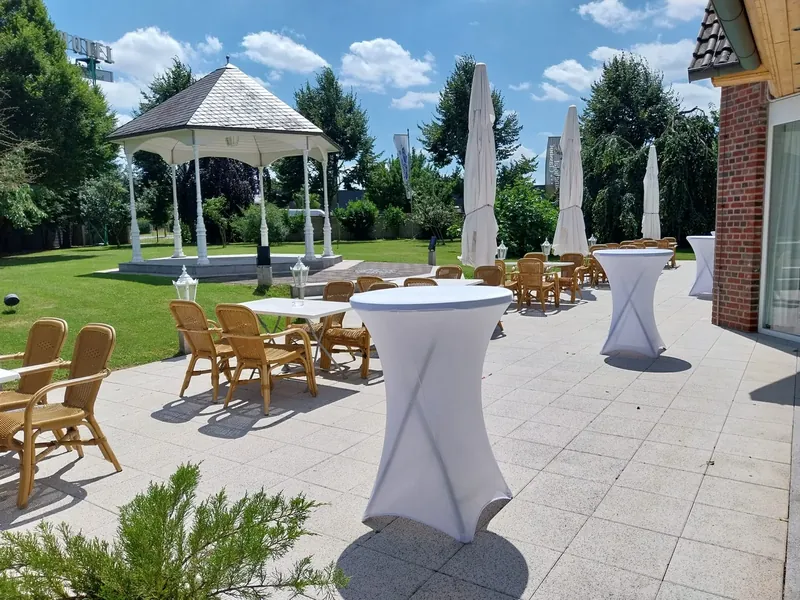 Reihe von Stehtischen mit weißen Hussen auf einer Terrasse, im Hintergrund ein Gartenpavillon