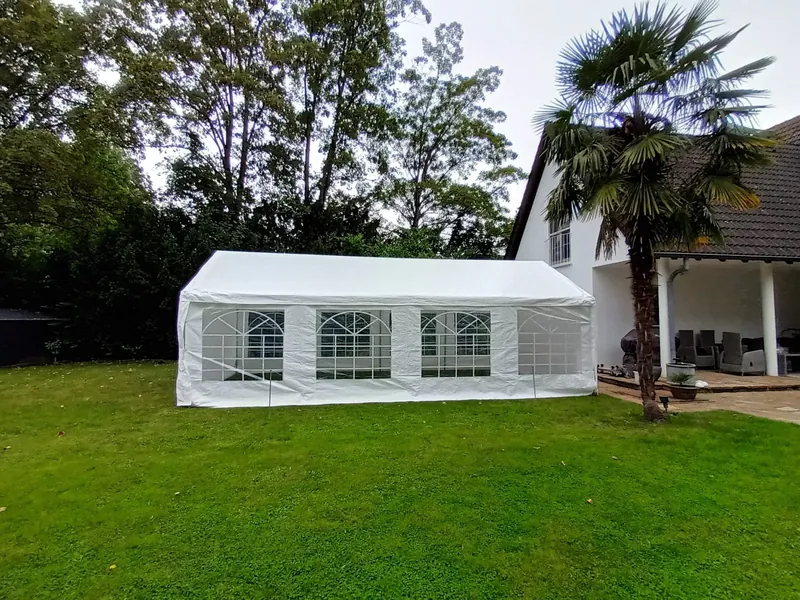 Aufgebautes weißes Partyzelt mit Fenstern auf einer Rasenfläche neben einem Wohnhaus